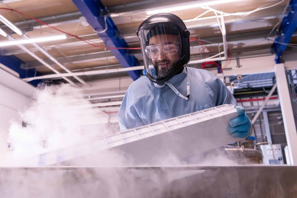 A scientist in PPE pulls out a sample rack from a liquid nitrogen tank