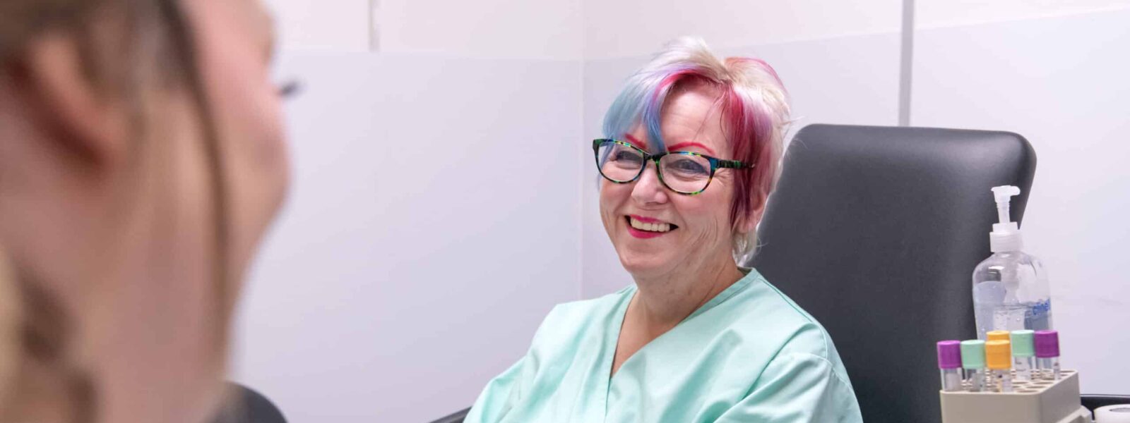 A participant smiles at a nurse, whilst sat next to sample tubes