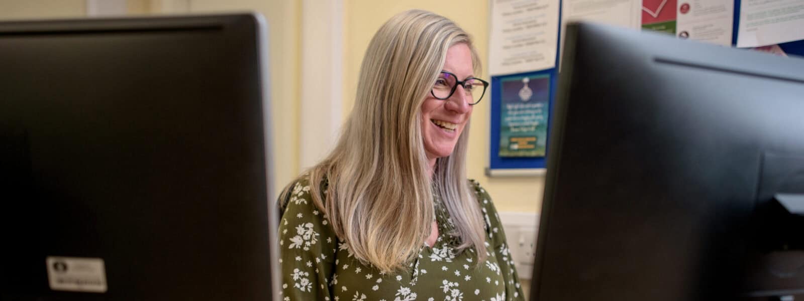 A woman on a computer at work smiles whilst looking at the screen