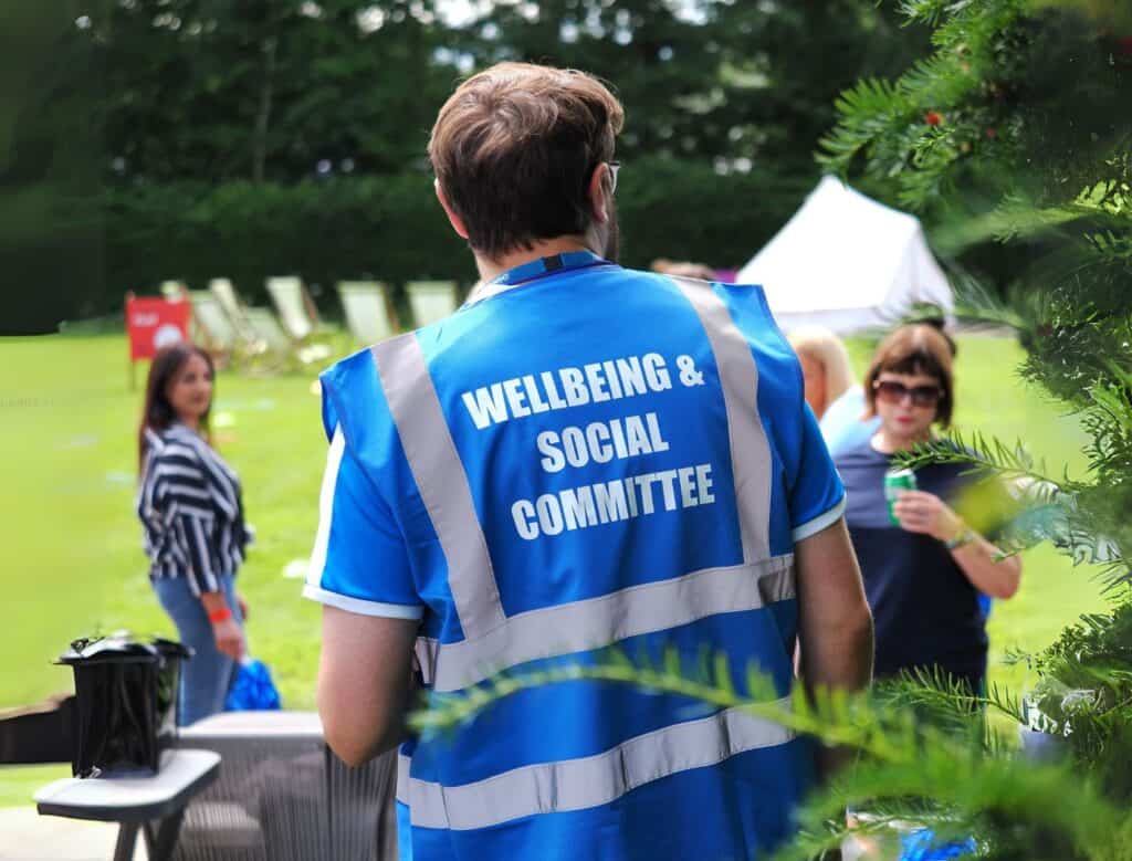 person oversees outdoor activities whilst wearing a high visibility vest that reads Wellbeing & Social Committee