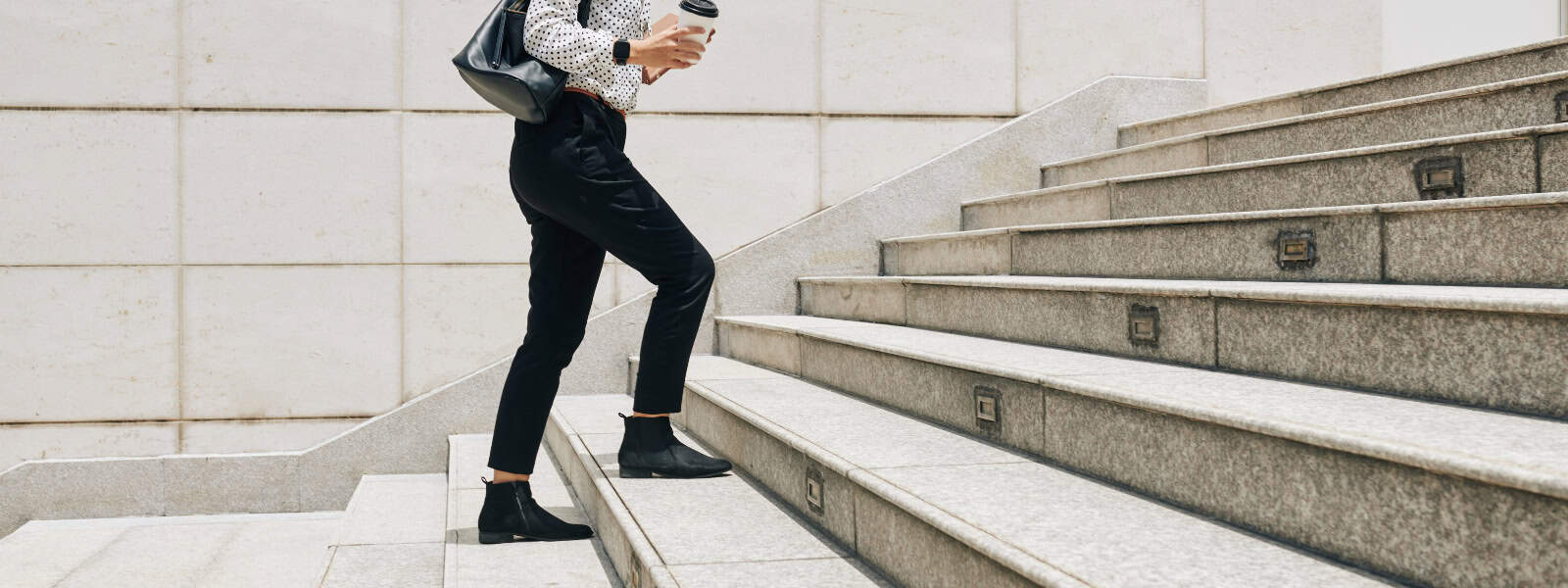 A woman walks up the stairs holding a coffee