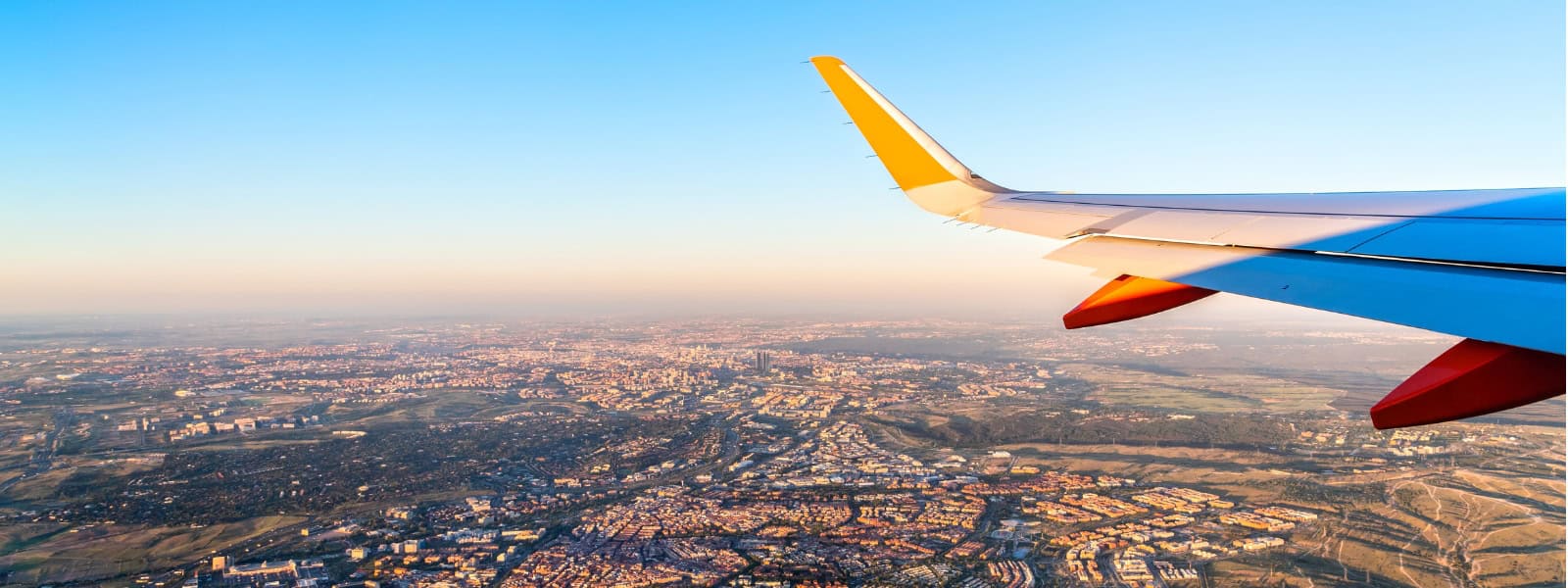 A shot out of a plane window of a wing of the plane passing over a town